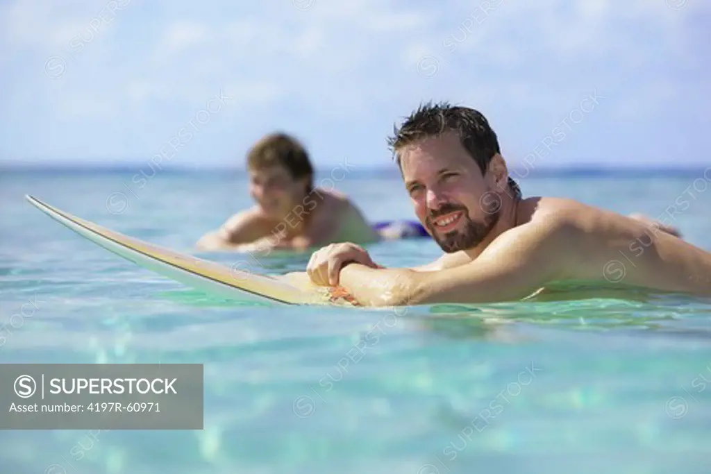 Surfer giving you a broad smile while floating on his surfboard in the waves