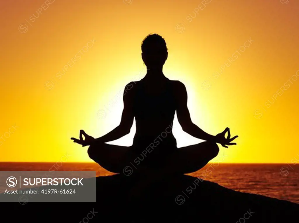 Silhouette of a woman doing yoga on the beach at sunset