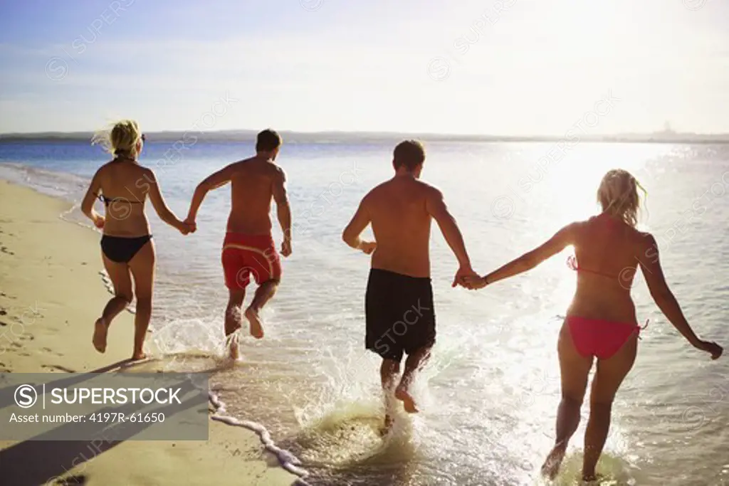 Two couples wearing swimwear and running into the ocean - rearview