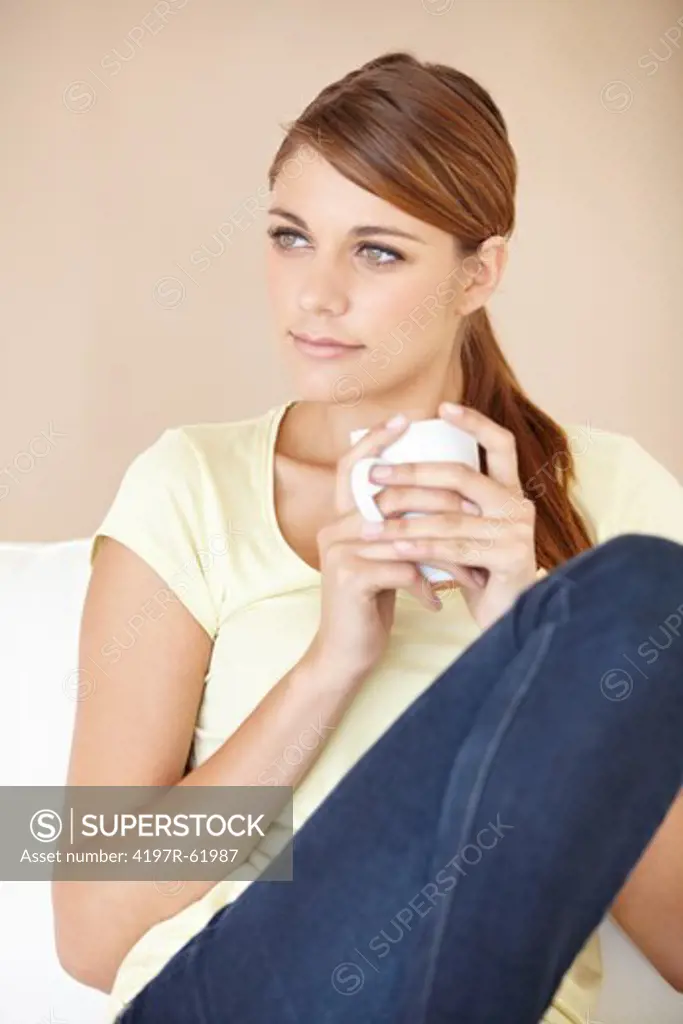 Shot of an thoughtful-looking young woman sitting and drinking a cup of coffee