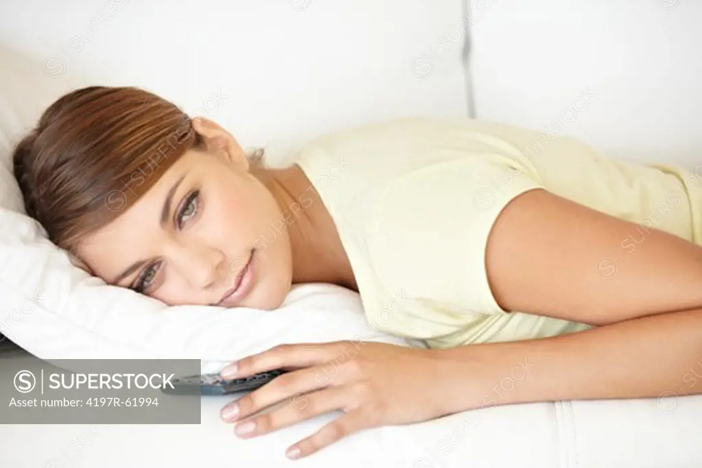 Portrait of a young woman looking bored while lying on a sofa watching TV