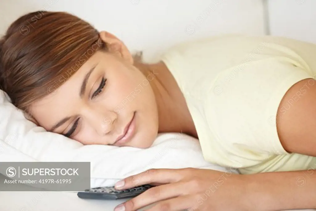 Shot of a young woman sleeping while lying on a sofa and holding a TV remote