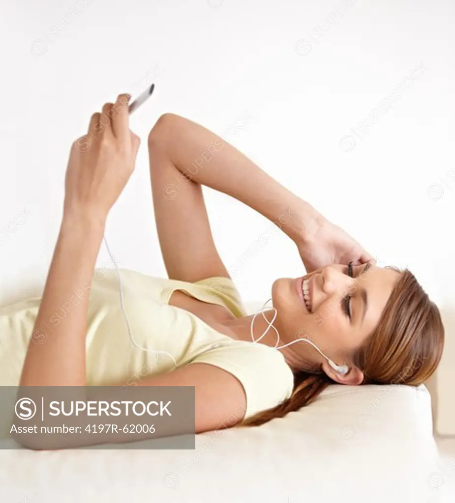 Shot of a young woman lying on her bed and listening to music on some earphones