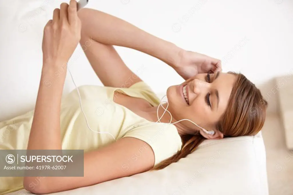 Shot of a young woman lying on her bed and listening to music on some earphones