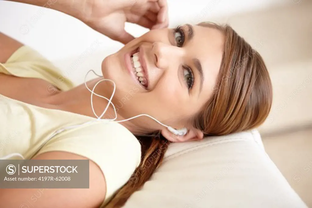 Closeup portrait of a young woman lying on her bed and listening to music on some earphones