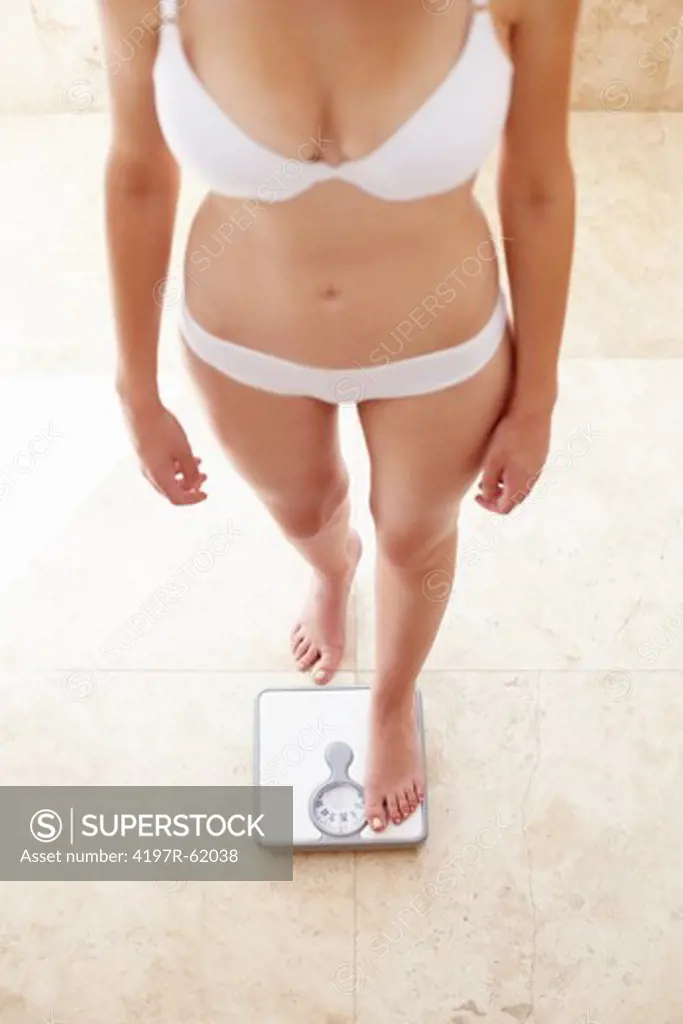 Cropped image of a young woman in her underwear weighing herself on the scale