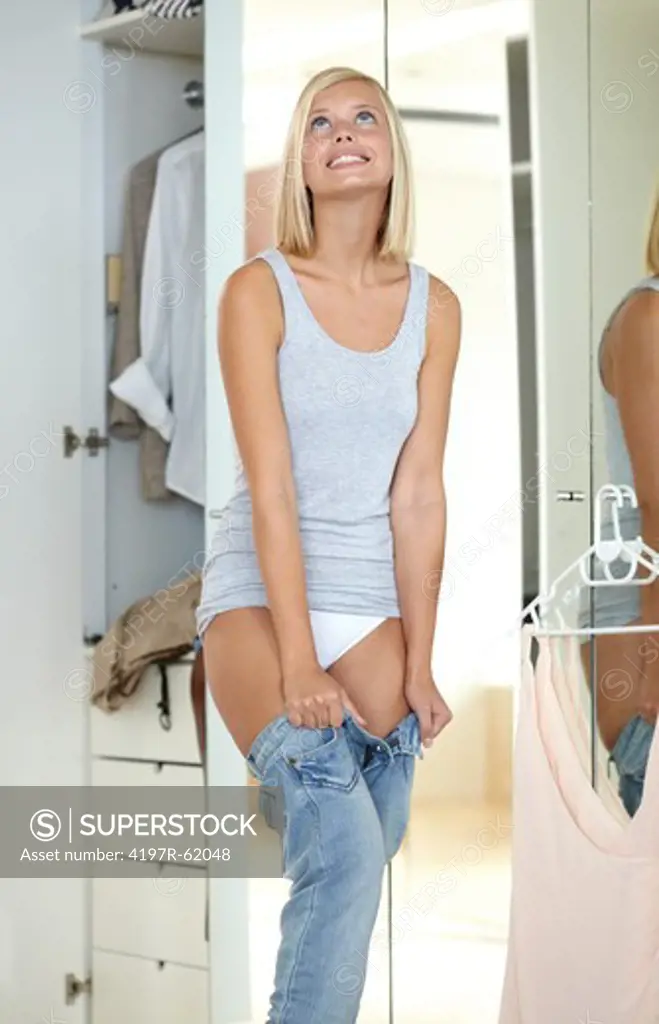 Shot of an attractive young girl standing in her bedroom and trying to pull on a tight pair of jeans