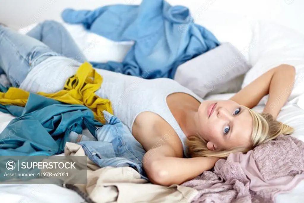 Portrait of an attractive young girl lying on her bed with clothing strewn about