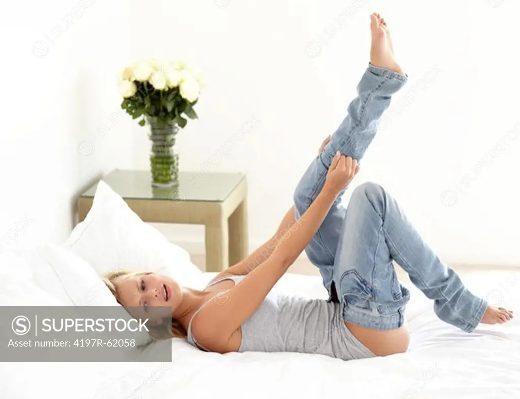 Shot of an attractive young woman lying on her bed and straining to pull on tight jeans