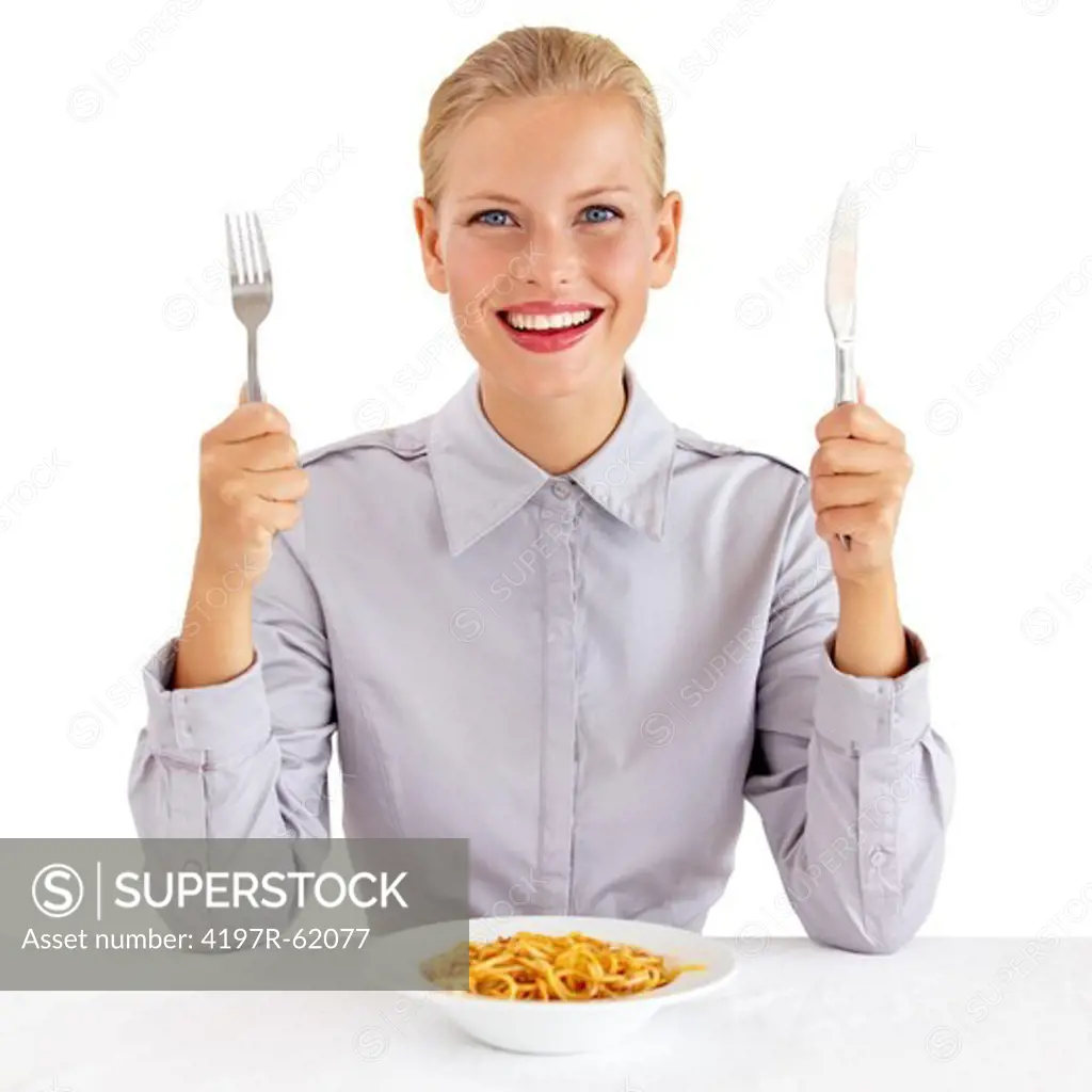 Portrait of a happy young woman holding a knife and fork with a bowl of paste infront of her