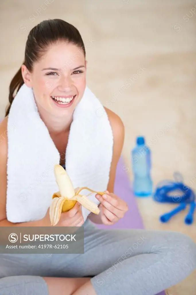 Fit young woman sitting on a yoga mat and peeling a banana