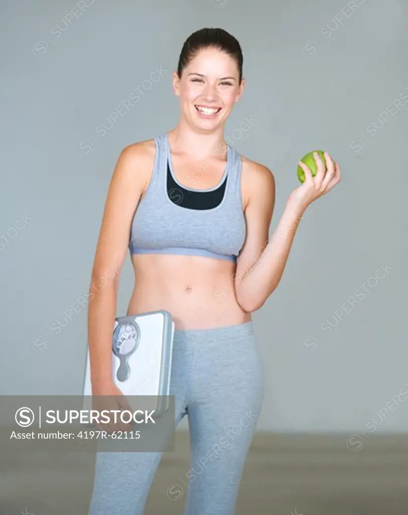 Cute young woman holding a fresh green apple and a scale