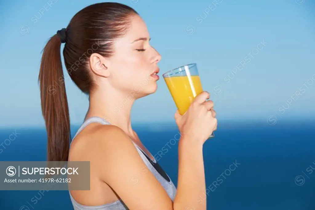 Profile of an attractive young woman drinking orange juice