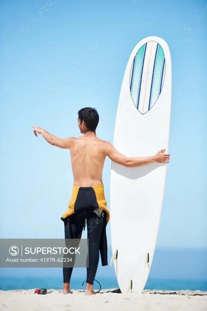 Rearview of young surfer in his wetsuit holding his surfboard while standing on a beach
