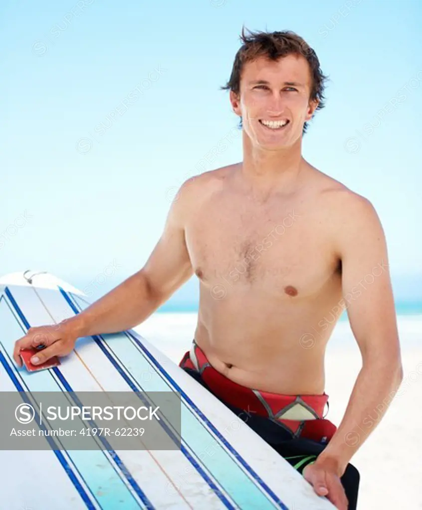 Portrait of a young surfer scraping the wax on his board with his credit card
