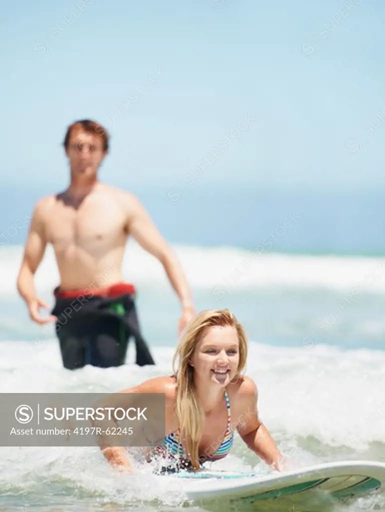 A pretty young blonde girl lying on a surfboard with a young man behind her