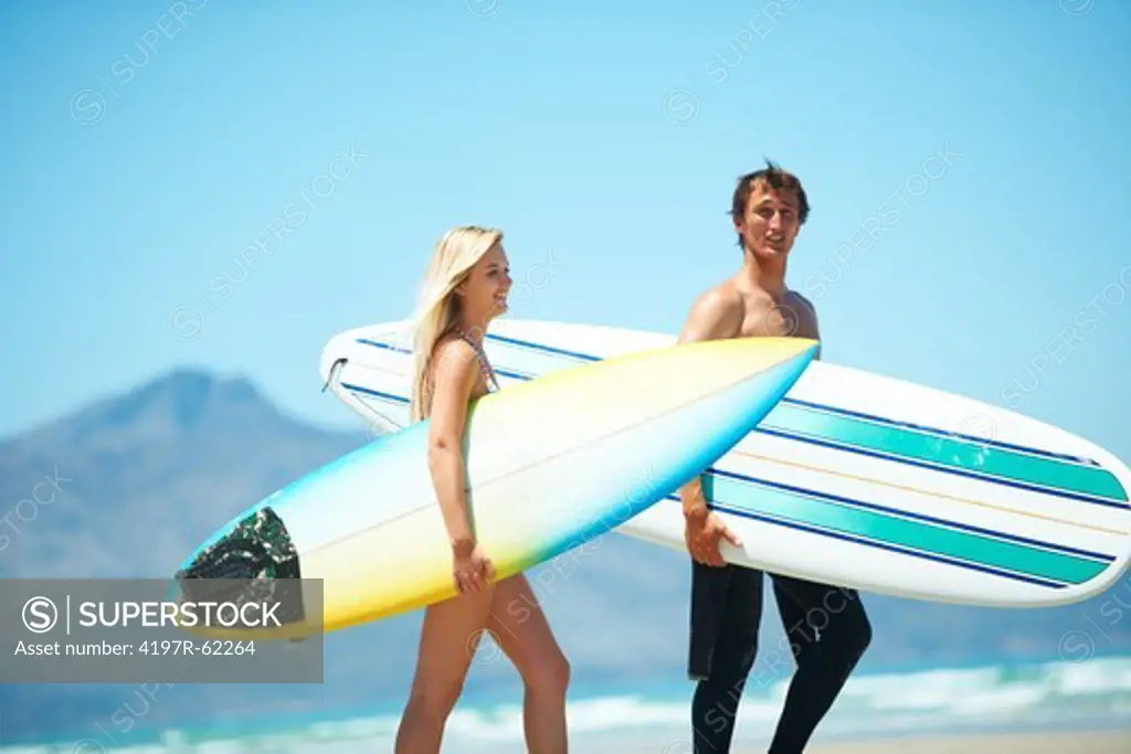 Two surfers walking on a beach carrying surfboards under their arms