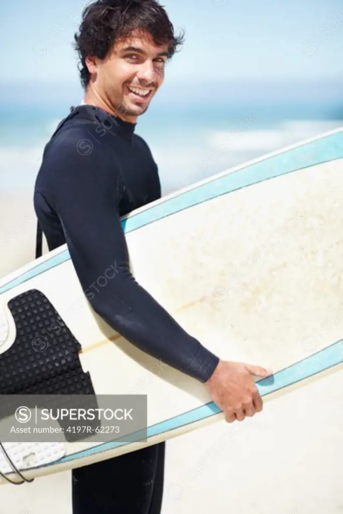 Portrait of a handsome surfer wearing a wetsuit and holding a surfboard while standing on a beach