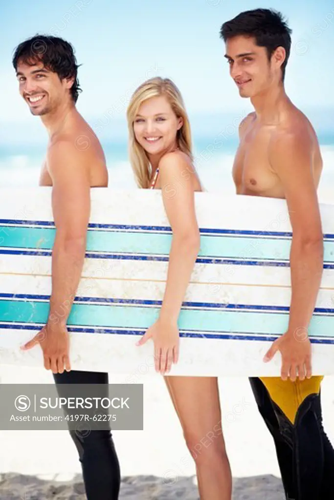 Profile of three surfers standing on a beach together and holding a surfboard