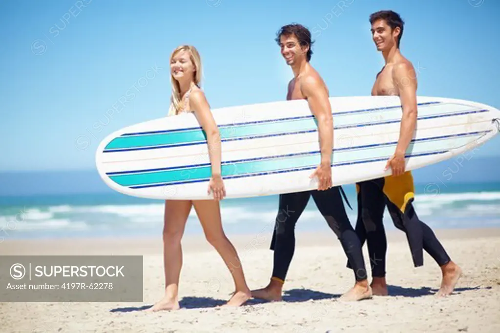 Three surfers carrying a surfboard together