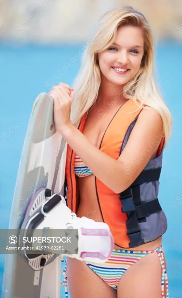 Portrait of a pretty young wakeboarder holding her board and wearing a life jacket
