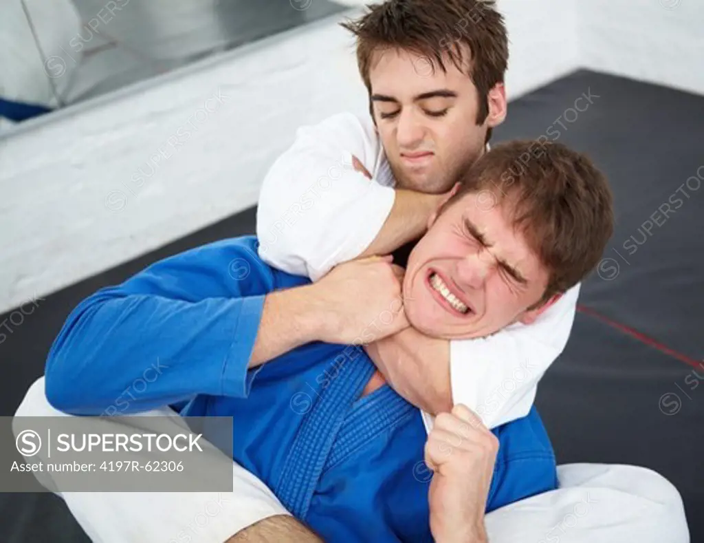 Shot of a young martial artist being choked while sparring with another in a dojo