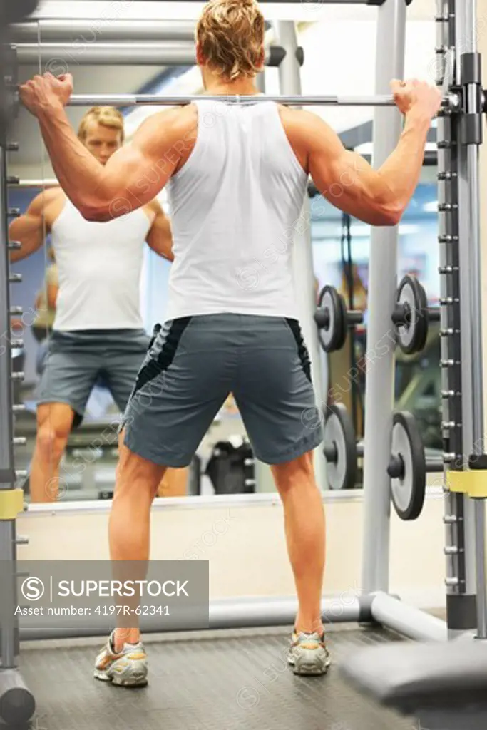 Full length rearview of a man doing shoulder presses in the gym