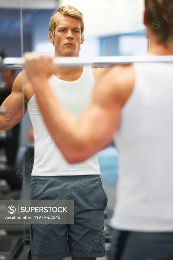 A young man standing infront of the mirror while weightlifting in the gym