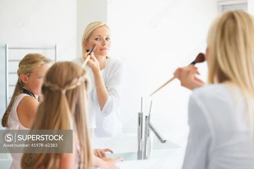 A mother shows her young daughter how to apply blush in the mirror