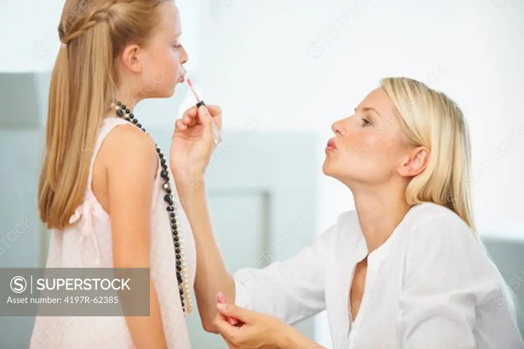 A mother applying lipgloss to her cute young daughter's face
