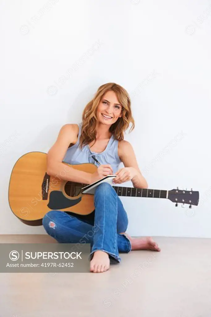 Smiling young woman sitting on the ground with her guitar and writing a song