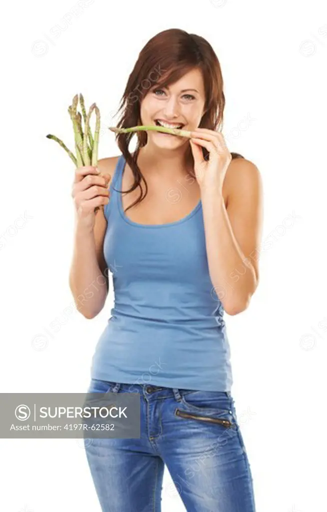 Studio portrait of an attractive young woman holding a bunch of asparagus spears and eating one isolated on white