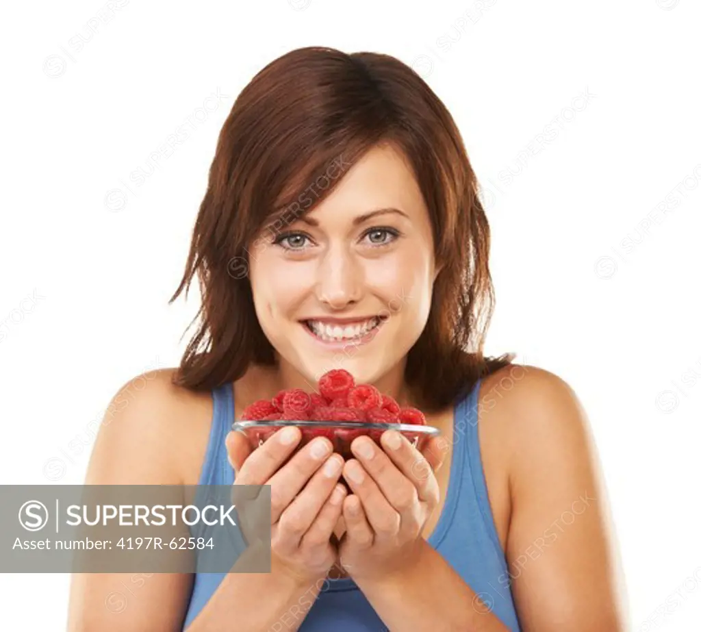 Studio portrait of an attractive young woman holding a bowl full of raspberries up to her face isolated on white