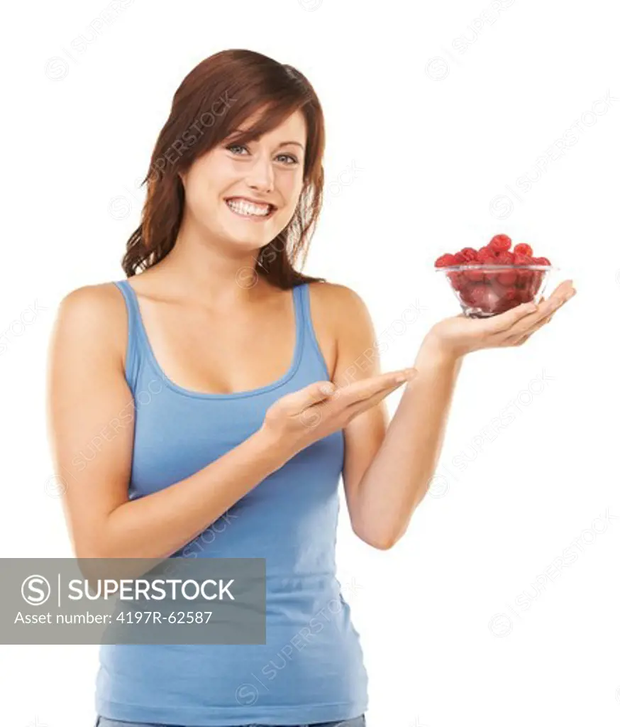 Studio portrait of an attractive young woman holding a bowl full of raspberries up and pointing to them isolated on white