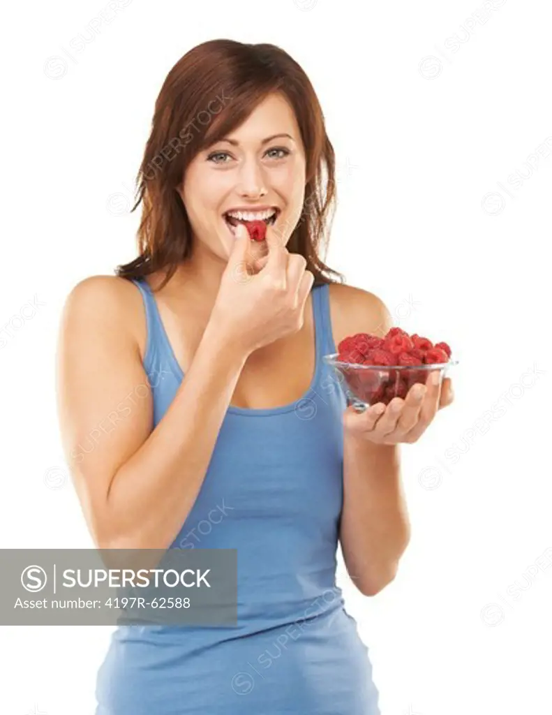 Studio portrait of an attractive young woman holding a bowl full of raspberries while eating one isolated on white
