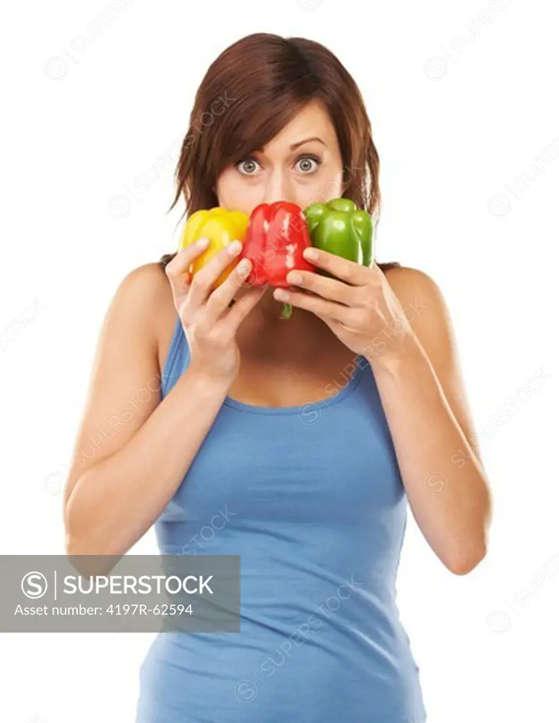 Studio shot of a young woman holding three colourful peppers in front of her face isolated on white