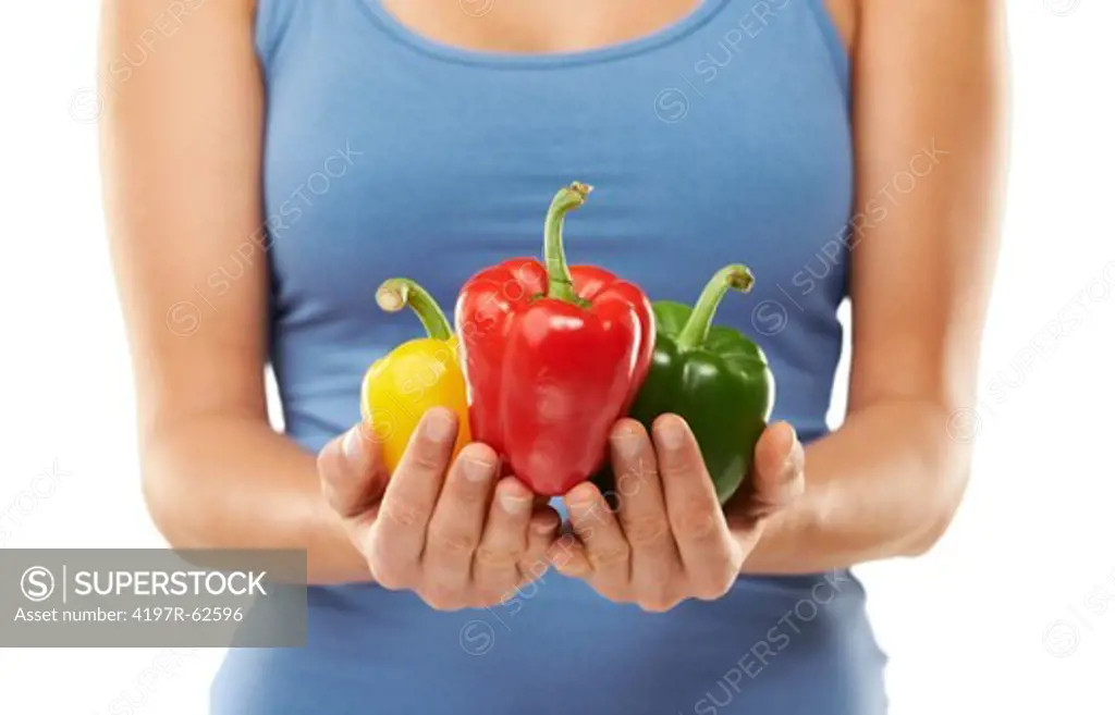 Cropped studio shot of a woman holding three colourful peppers in front of her isolated on white