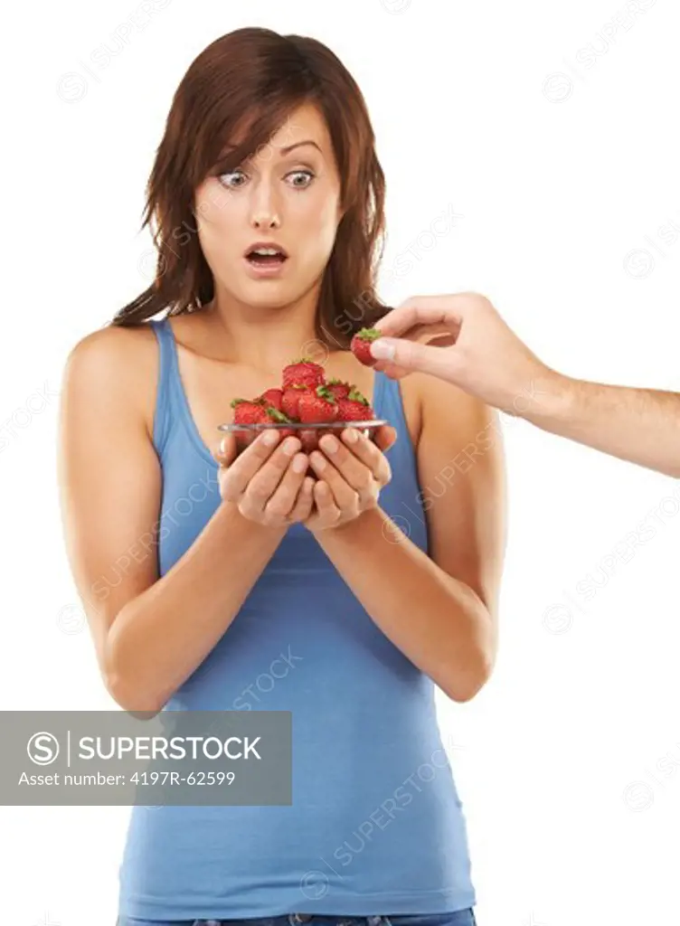 Studio shot of a shocked-looking young woman holding a bowl of strawberries while an arm steals one from outside of the frame isolated on white