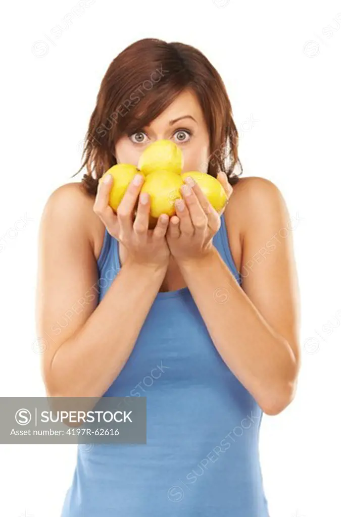 Playful studio portrait of a young woman holding up a bunch of lemons in front of her face isolated on white