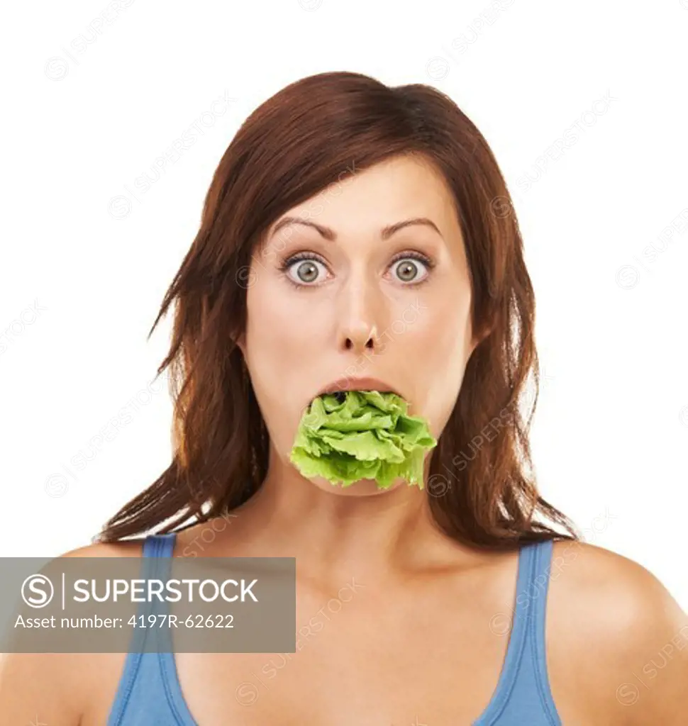 Studio portrait of a shocked-looking young woman with her mouth stuffed full of lettuce leaves isolated on white