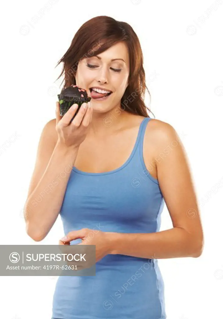 Studio portrait of a young woman holding a chocolate cupcake and licking it isolated on white