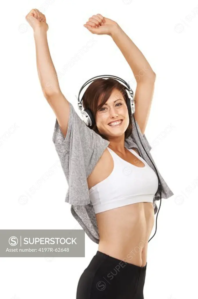 Sideways studio shot of a sporty young woman wearing headphones and dancing with her arms over her head isolated on white