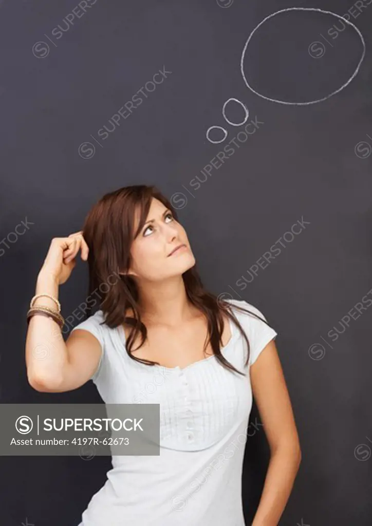 Studio concept shot of a confused young woman looking up at a thought bubble drawn on a blackboard above her head