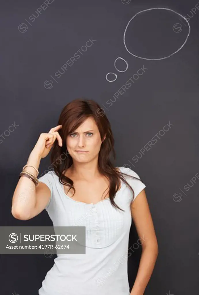 Studio concept portrait of a confused young woman scratching her head  with an empty thought bubble drawn on a blackboard above her