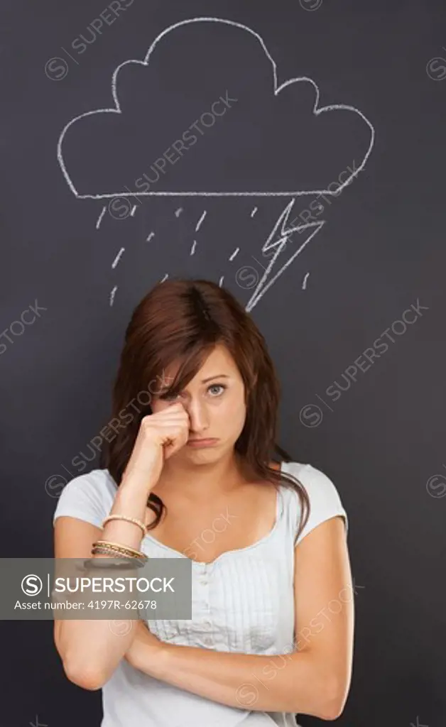 Studio concept portrait of a sad-looking young woman with a chalk drawing of a stormy weather drawn on a blackboard above her head