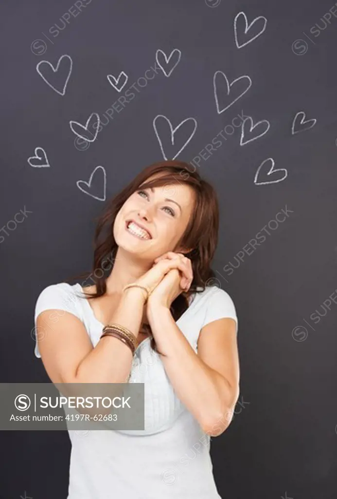 Studio concept shot of an happy-looking young woman daydreaming about love with many hearts drawn on a blackboard above her head