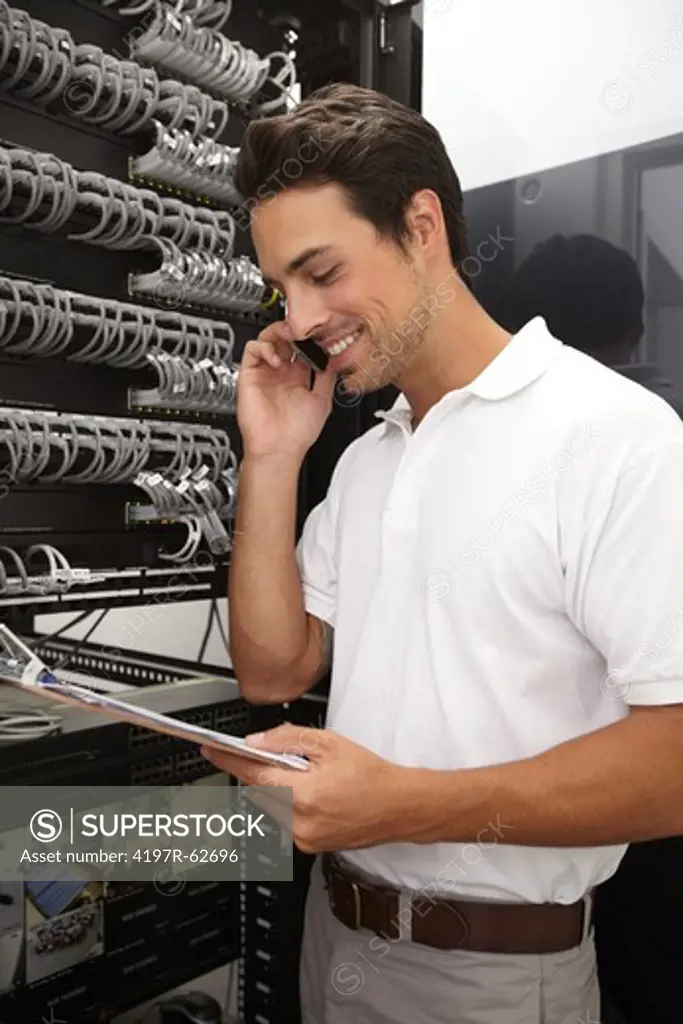 Young IT technician working in a server room while taking a call on his mobile