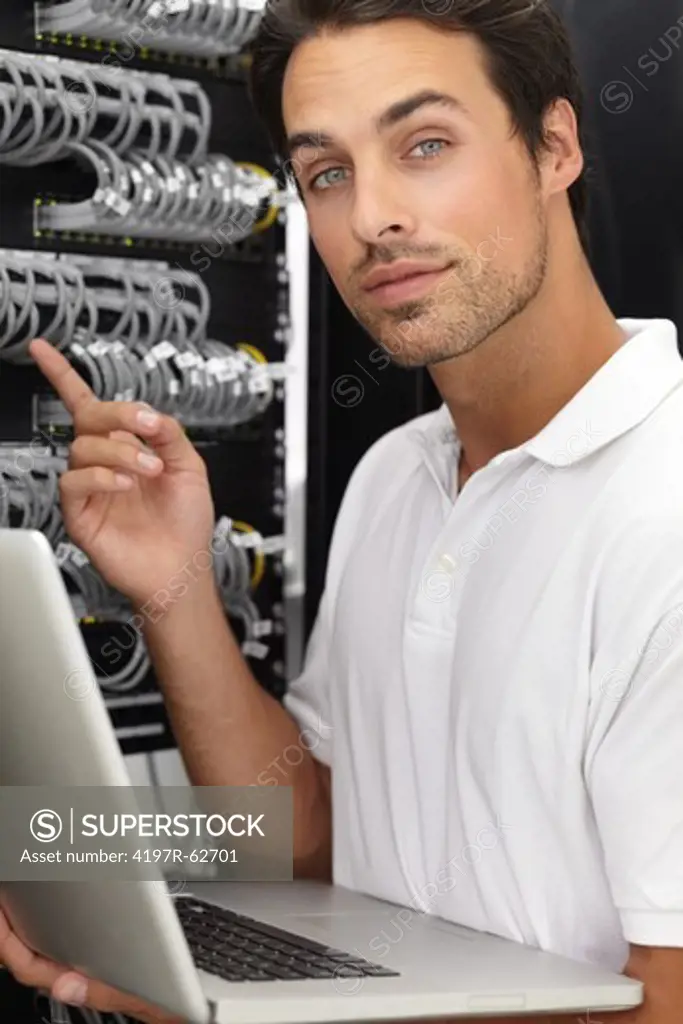 Young IT consultant working in a server room on his laptop while pointing at something