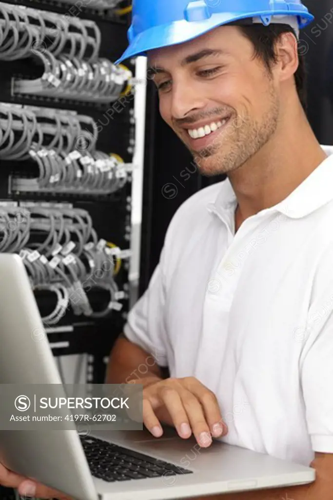 Smiling young IT consultant working in a server room on his laptop