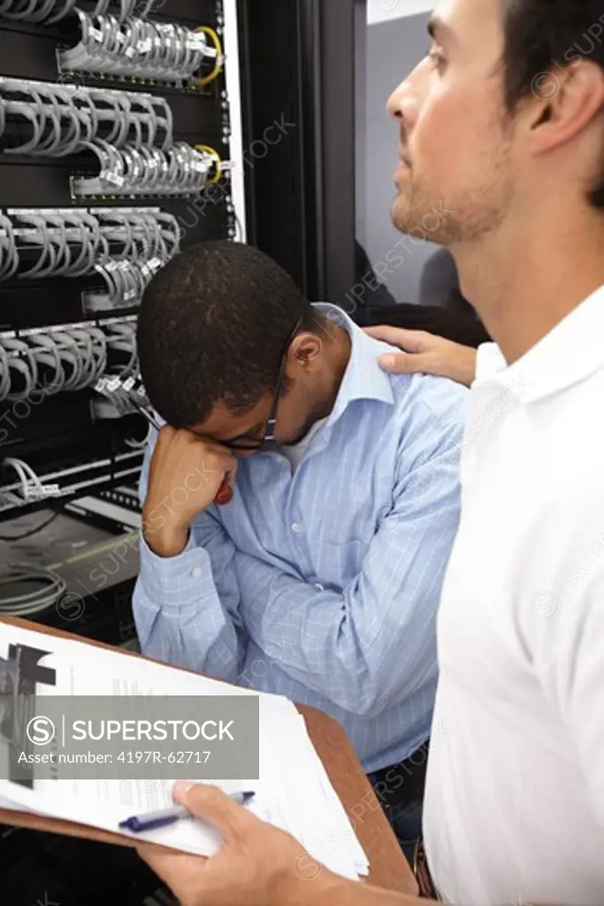 Demoralized young IT consultant working in a server room with a coworker